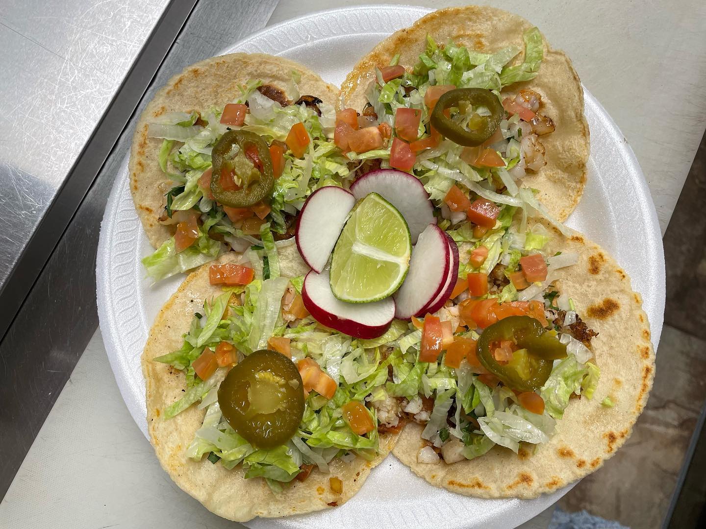 Shrimp tacos arranged with lime, radish and jalapeno on a plate
