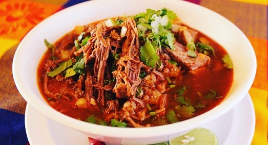 A bowl of birria de res with cilantro and onion