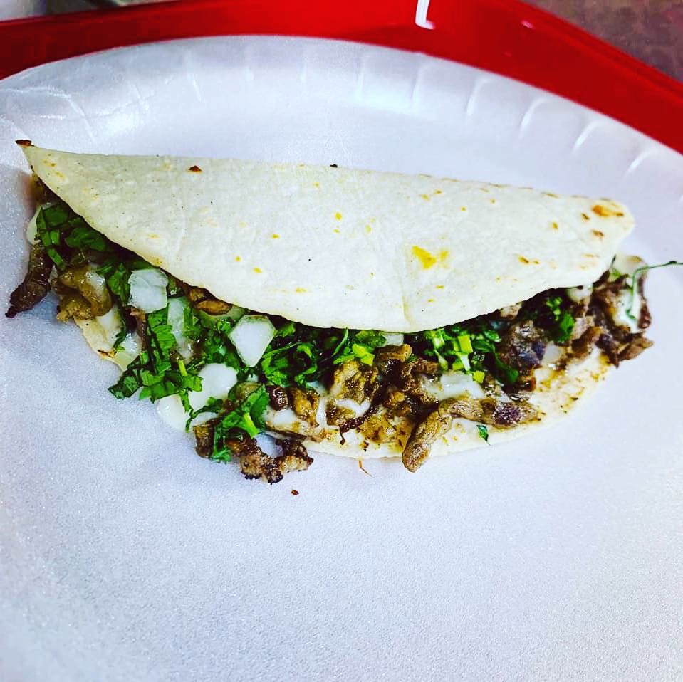 A close-up quesabirria taco with melted cheese on a paper plate